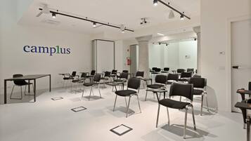 A modern conference room with a white ceiling, black chairs, and tables. The word "campus" is visible on the wall.