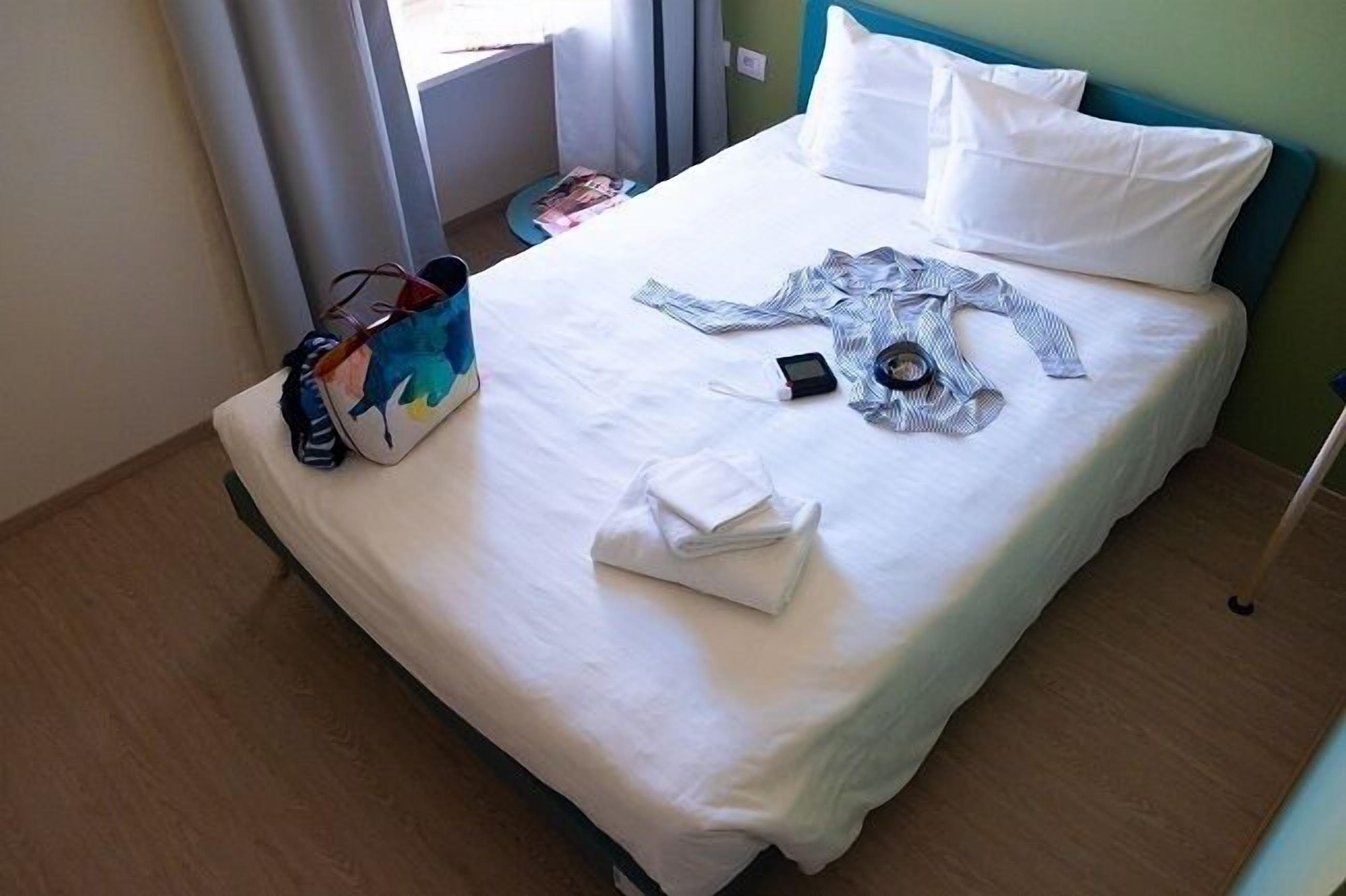 Une chambre d’hôtel avec un lit, une valise, une serviette pliée et un téléphone portable posé sur le lit.