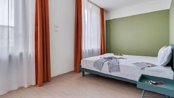 Une chambre d’hôtel avec un lit, une tête de lit verte et des rideaux.
