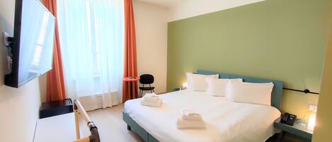 Ein Hotelzimmer mit Bett, Fernseher, Sessel, Schreibtisch und Rollstuhl.