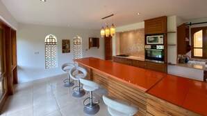 A modern kitchen with a large island, bar stools, and a microwave. - Villa 47 Vipingo Ridge (Vipingo)