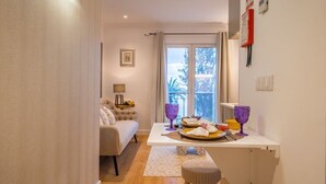 Kompakti hotellihuone, jossa on sänky, pieni oleskelualue, ruokapöytä ruokatarjottimella ja ikkuna, josta avautuu näkymä puita kohti.