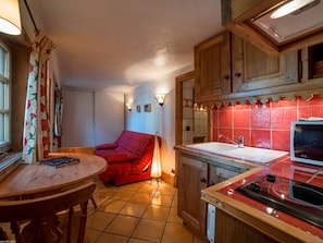 Een keuken met een rode stoel, een eettafel en een fornuis.