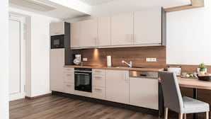 Een moderne keuken met houten vloeren, witte kasten, een ingebouwde oven, een koffieapparaat en een eethoek met een stoel en tafel.