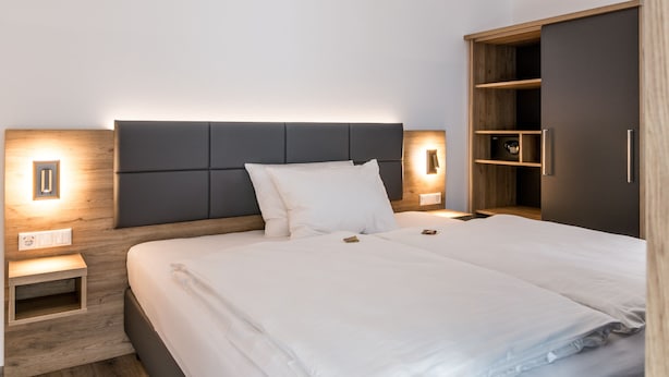 Een moderne hotelkamer met een groot bed, een nachtkastje, een garderobe en een wandlamp.