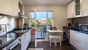 Une cuisine moderne équipée d’un lave-linge, un coin repas avec une table et des chaises, et une vue à travers une porte vitrée.