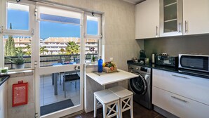 Une cuisine compacte équipée d’un lave-linge, d’un four à micro-ondes et d’une petite table sur laquelle se trouve un panier de fruits.