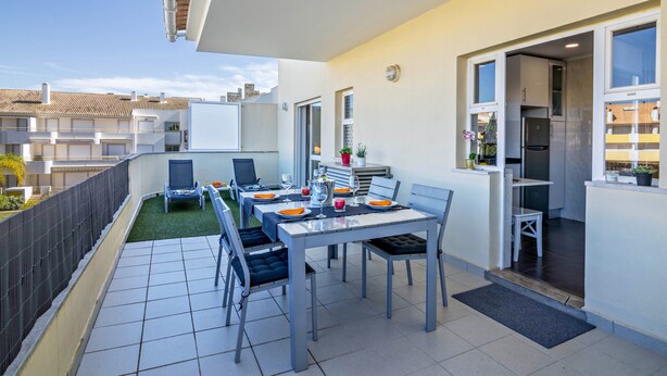 Un balcon avec une table à manger pour quatre personnes, un petit coin jardin et une vue sur les bâtiments voisins.