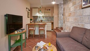 Un salon avec un téléviseur, un canapé, une table basse avec un livre et un verre de jus de fruits, et un coin cuisine avec une table à manger et des chaises.