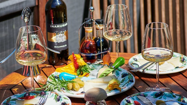 Une table en bois, sur laquelle on trouve des bouteilles de vin, des verres et des assiettes remplies de nourriture.