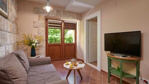 Un salon chaleureux avec un canapé, une petite table sur laquelle se trouve un plateau de nourriture, un téléviseur posé sur un meuble et un mur en pierre.
