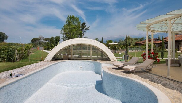 A swimming pool with a curved glass enclosure, lounge chairs, and a pergola with umbrellas. - ❤️Luxury Villa with pool. NEW❤️ (pietrasanta)