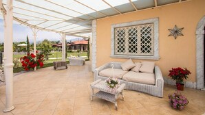 A covered outdoor seating area with a wicker sofa, a small table with flowers, and potted plants. - ❤️Luxury Villa with pool. NEW❤️ (pietrasanta)