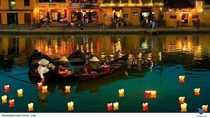 A traditional building with a balcony, a reflection in the water, and a boat with people. - Hoian Royal Villa (Da Nang)
