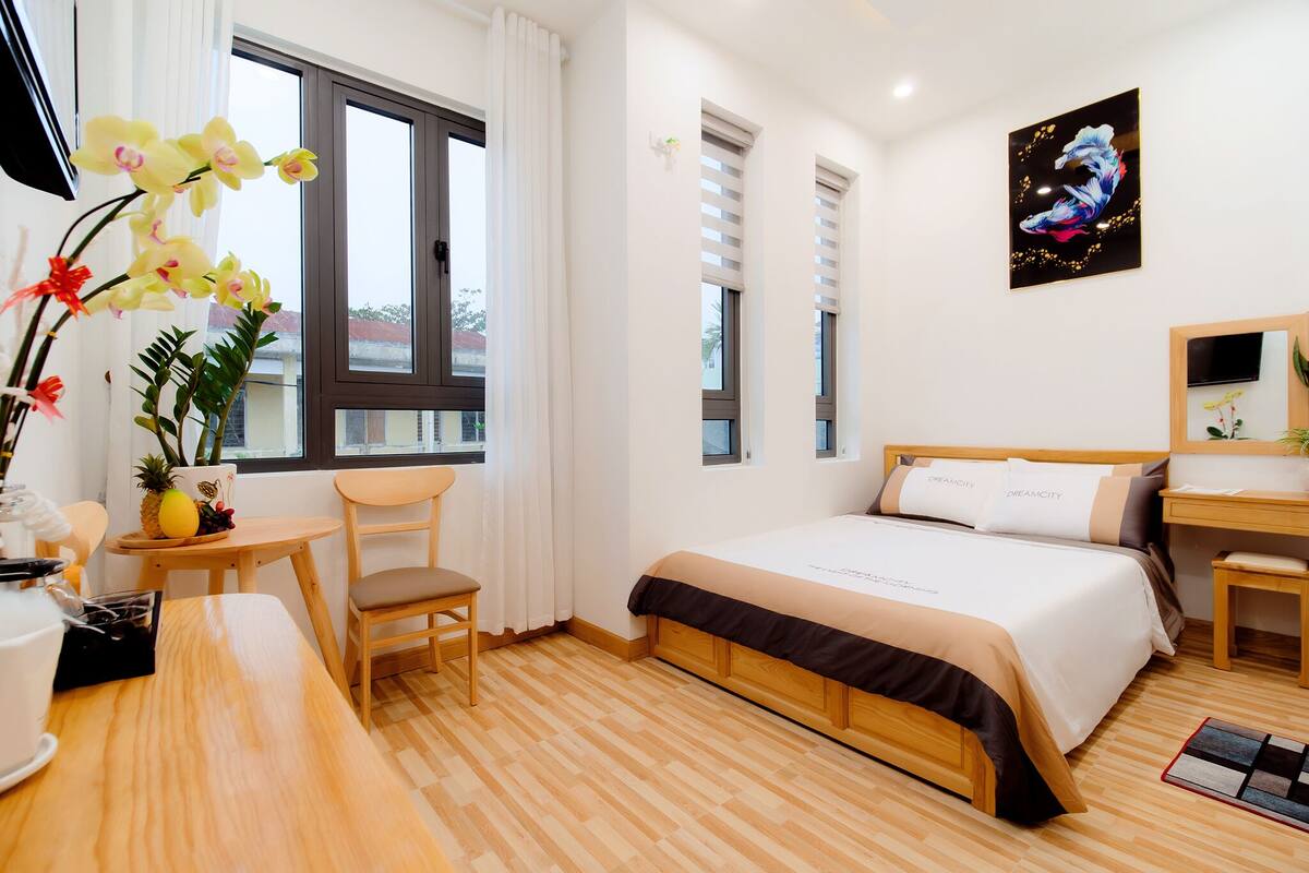 A hotel room with a bed, a desk, a chair, a small table, and a window with curtains.