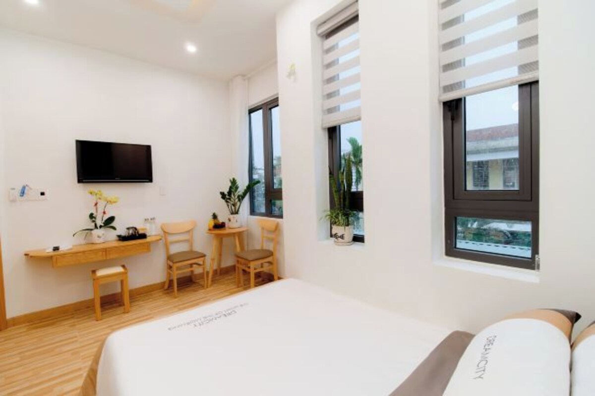 Ein modernes Hotelzimmer mit Bett, Schreibtisch, zwei Stühlen, Fernseher und großen Fenstern.