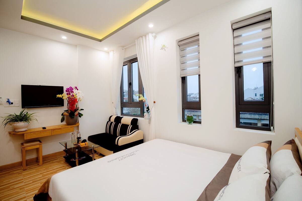 A hotel room with a bed, a desk, a chair, a TV, and windows with blinds.