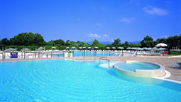 Uma grande piscina ao ar livre com várias pistas de natação, rodeada por espreguiçadeiras e guarda-sóis.