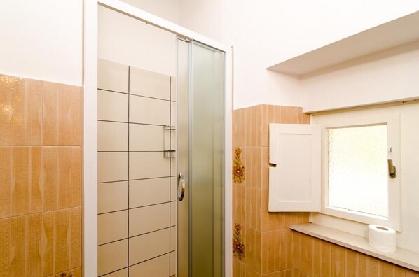 A bathroom with a glass shower door, a toilet, and a window with a frosted glass pane. - Holiday Home Patricija (Dubrovnik)