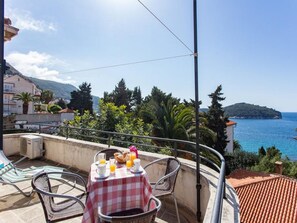 A balcony with a table set for breakfast, overlooking a coastal view with buildings and trees. - Holiday Home Patricija (Dubrovnik)
