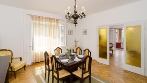 Een eetkamer met een houten tafel voor vier personen, een kroonluchter en een groot raam met gordijnen.