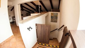 Un escalier avec une rampe en bois, un mur blanc orné d’un tableau et un sol carrelé.