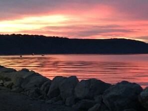 Un lago tranquilo al atardecer con una orilla rocosa en primer plano.