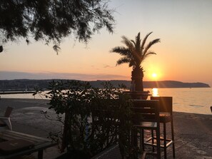 A beach setting with a palm tree, chairs, and a view of the sunset over water. - Apartment Fontana_next to Beach & Free Parking (Izola)