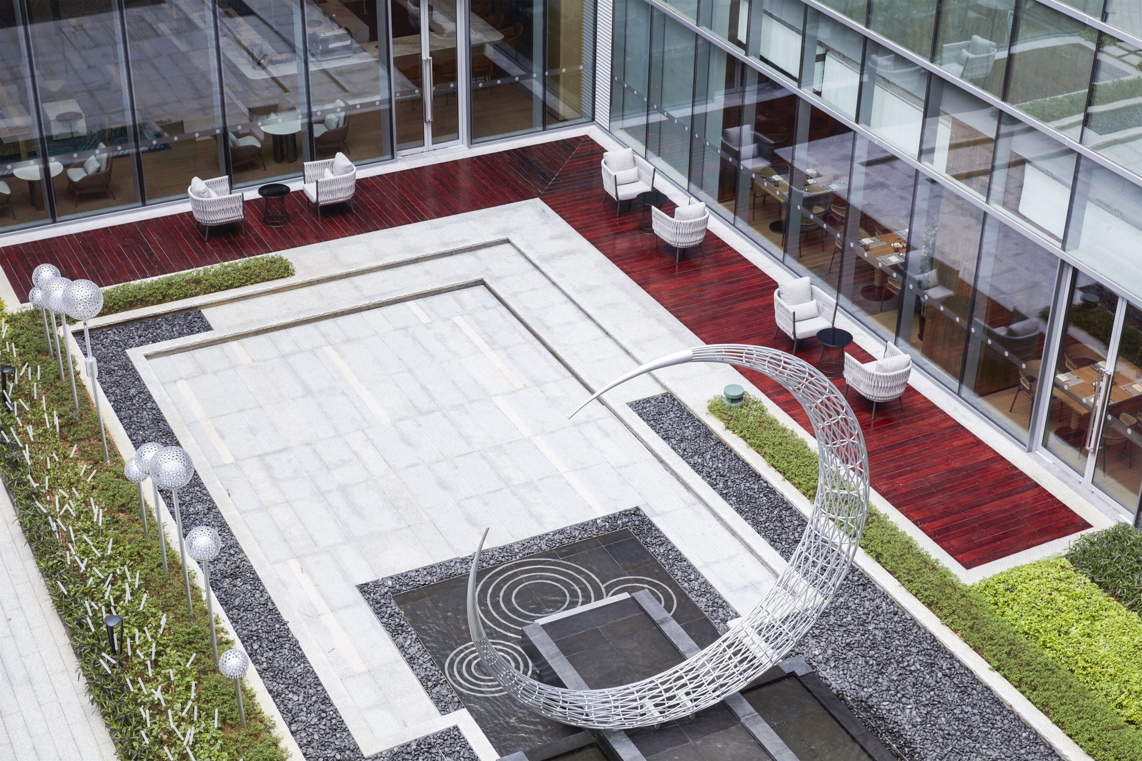 A modern outdoor seating area with white chairs and a unique curved white structure, surrounded by glass walls and a red carpeted floor.