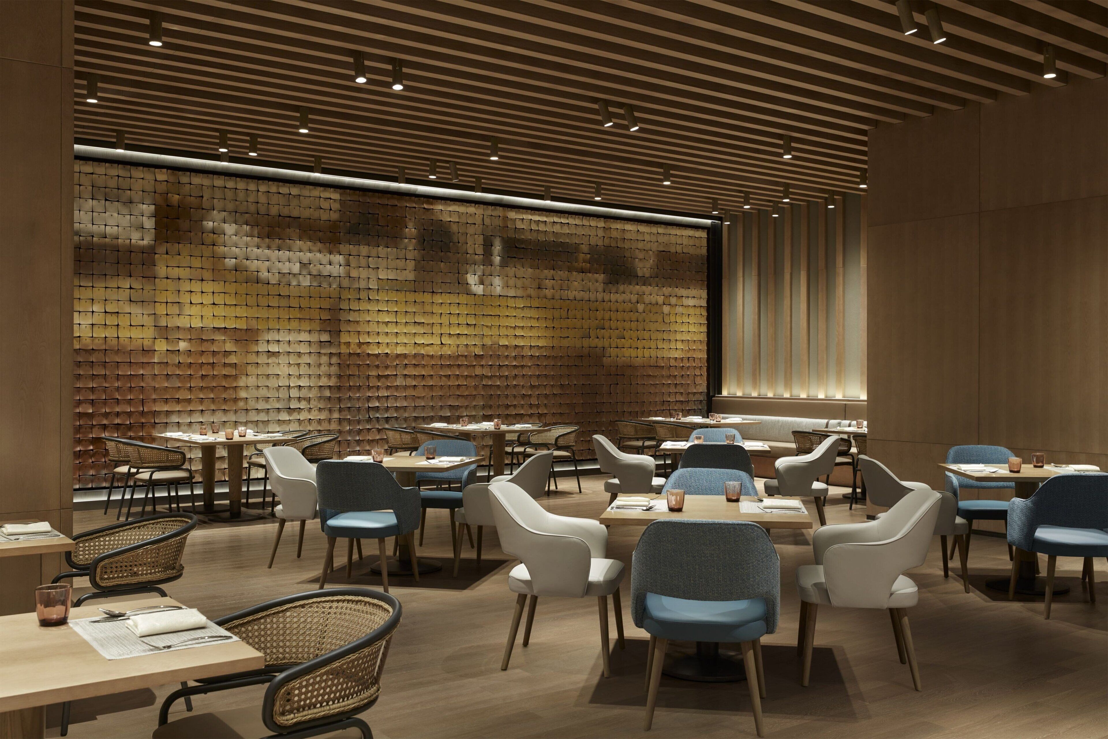A modern restaurant interior with wooden panel walls, round tables, and a variety of chairs.