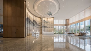 Eine großzügige Lobby mit poliertem Marmorboden, einem Empfangsbereich und einem großen Fenster mit Blick ins Freie.