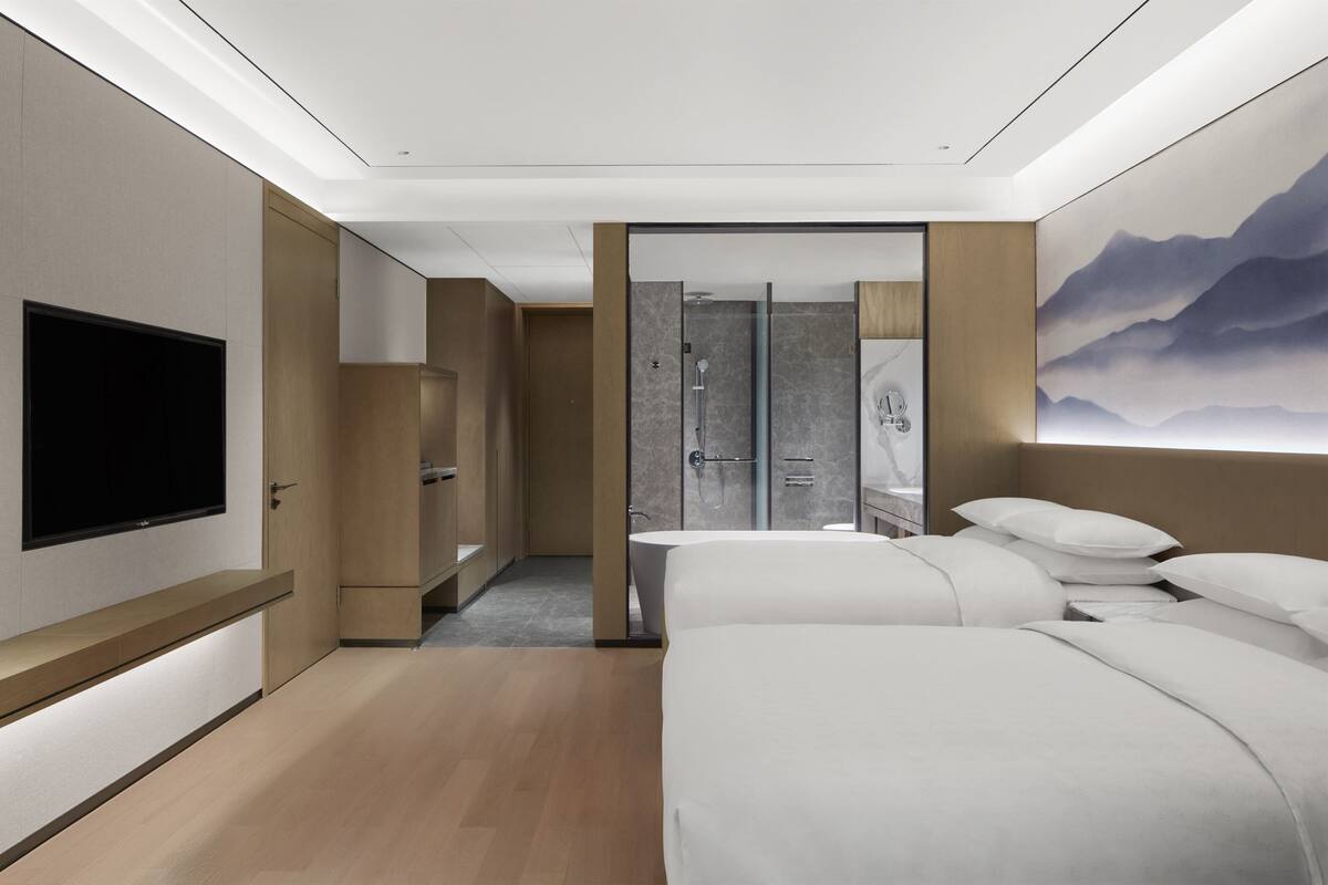 A modern hotel room with a large bed, a flat-screen TV, a walk-in closet, and a bathroom with a shower and mirror.