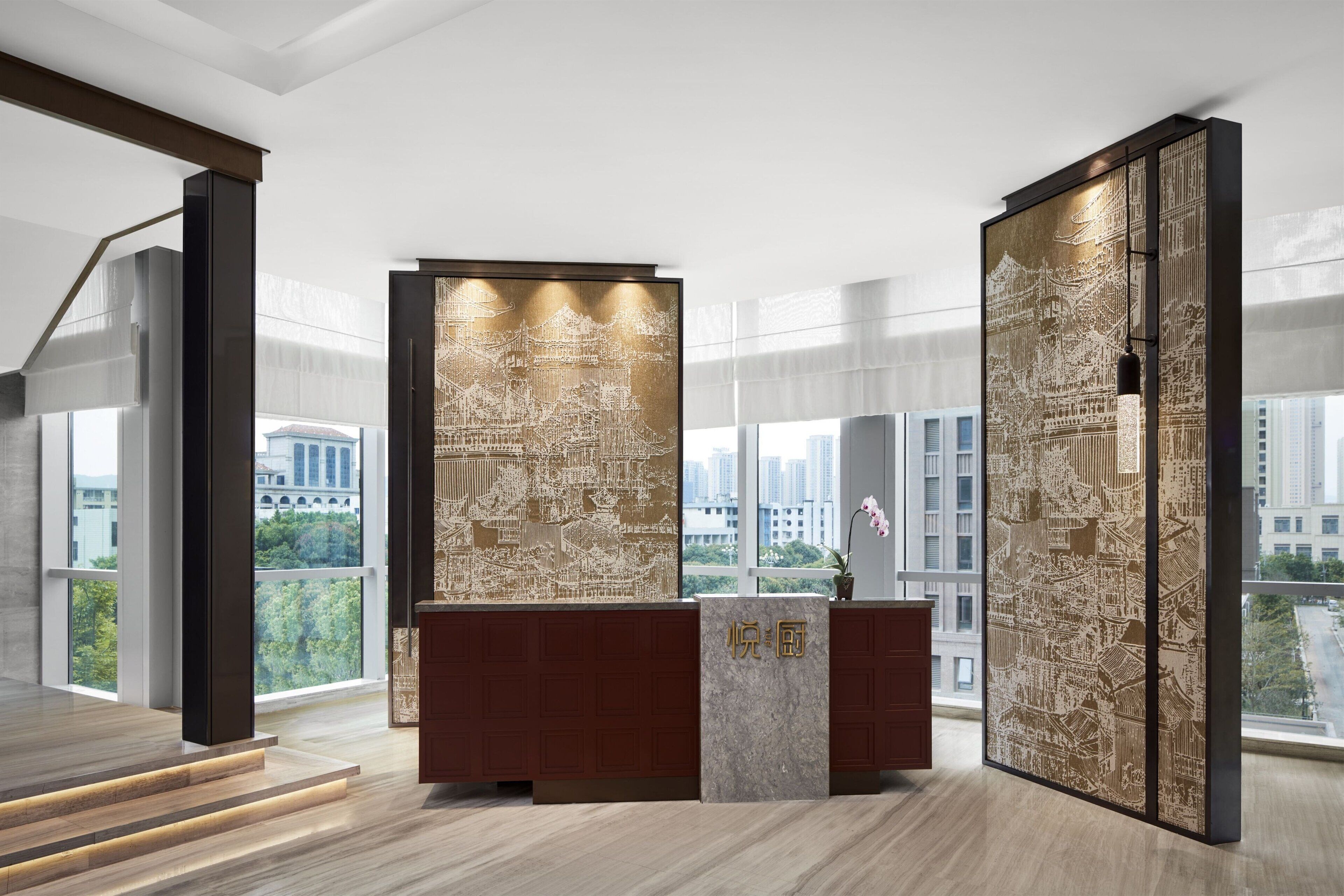 Una moderna hall d'hotel con una reception in legno, ampie finestre che offrono vista sulla città e pannelli decorativi con motivi elaborati.