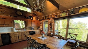A rustic kitchen with wooden cabinets, a large dining table, and a chandelier. - Enjoy this 100+ year old cabin in the gated Wolf Laurel Resort community. (MARS HILL)