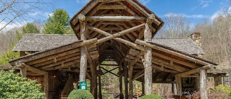 A rustic log cabin with a steeply pitched roof, a central chimney, and a stone foundation.