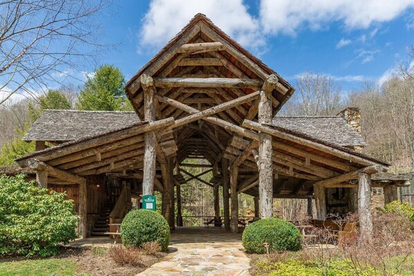 A rustic log cabin with a steeply pitched roof, a central chimney, and a stone foundation.