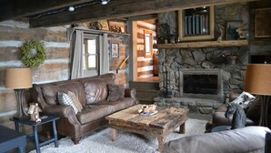 A cozy living room with a stone fireplace, leather sofa, and rustic decor. - Enjoy this 100+ year old cabin in the gated Wolf Laurel Resort community. (MARS HILL)
