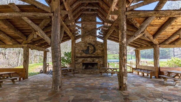 A rustic stone patio with wooden benches and a stone fireplace. - Enjoy this 100+ year old cabin in the gated Wolf Laurel Resort community. (MARS HILL)