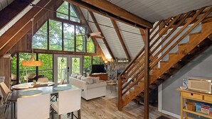 Spazioso loft con soffitto alto, travi in legno, una scala, zona pranzo e soggiorno con divano e TV.
