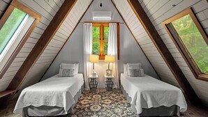 Una camera da letto mansardata accogliente con due letti, un'ampia finestra e una lampada centrale.