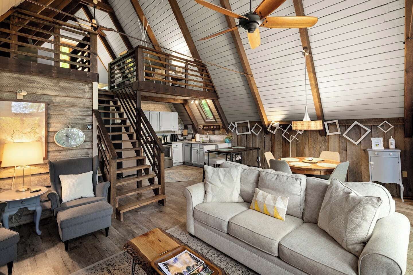 A loft-style living space with a wooden staircase, a sofa, a coffee table, and a dining area.