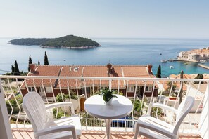 A balcony with white chairs and a small table, overlooking a coastal town with terracotta-roofed buildings and a clear view of the sea. - Beautiful Nest Rooms (Dubrovnik)