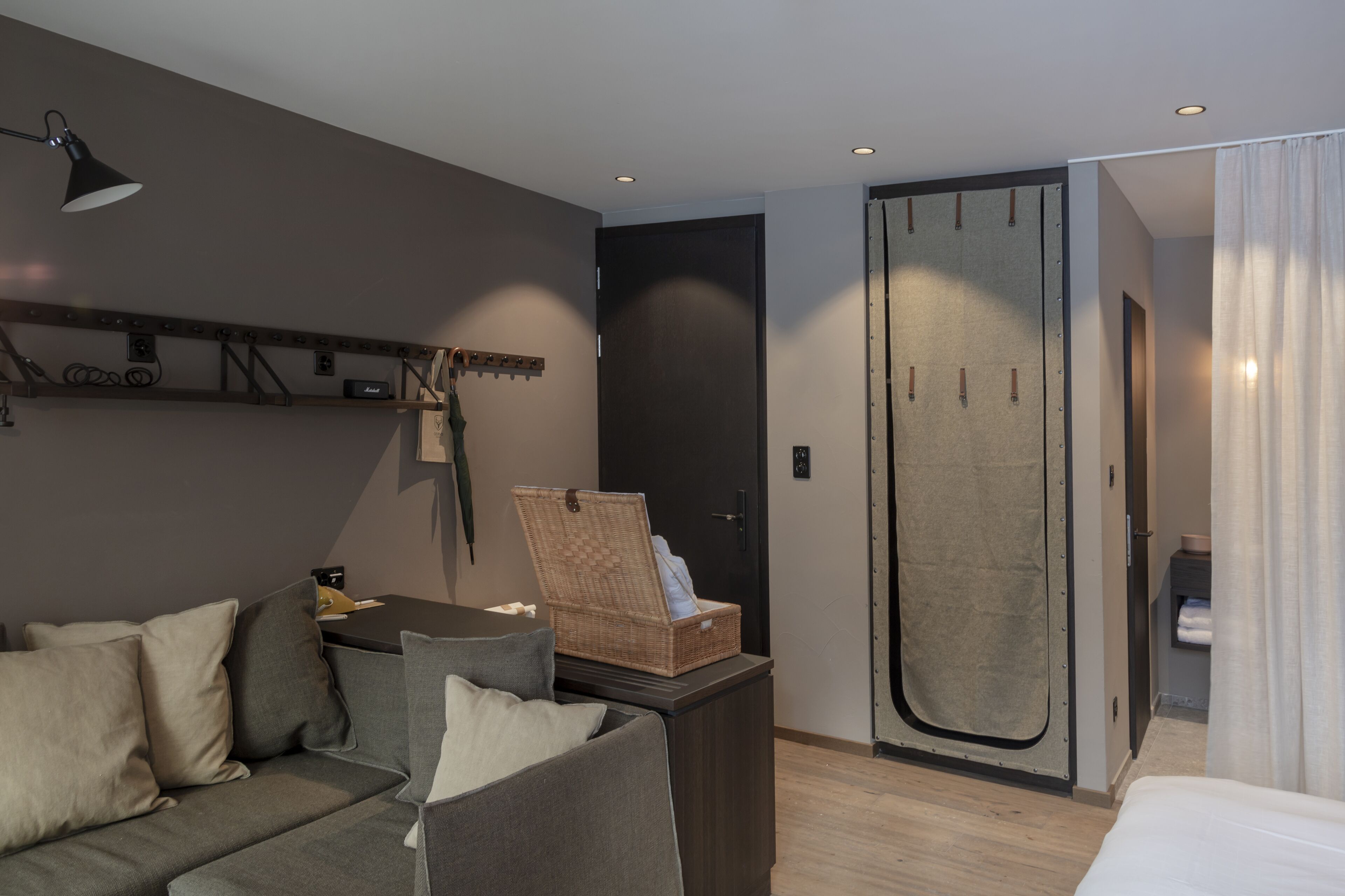 Une chambre d’hôtel moderne avec un canapé, une petite table, un panier en osier, une armoire et un lit.