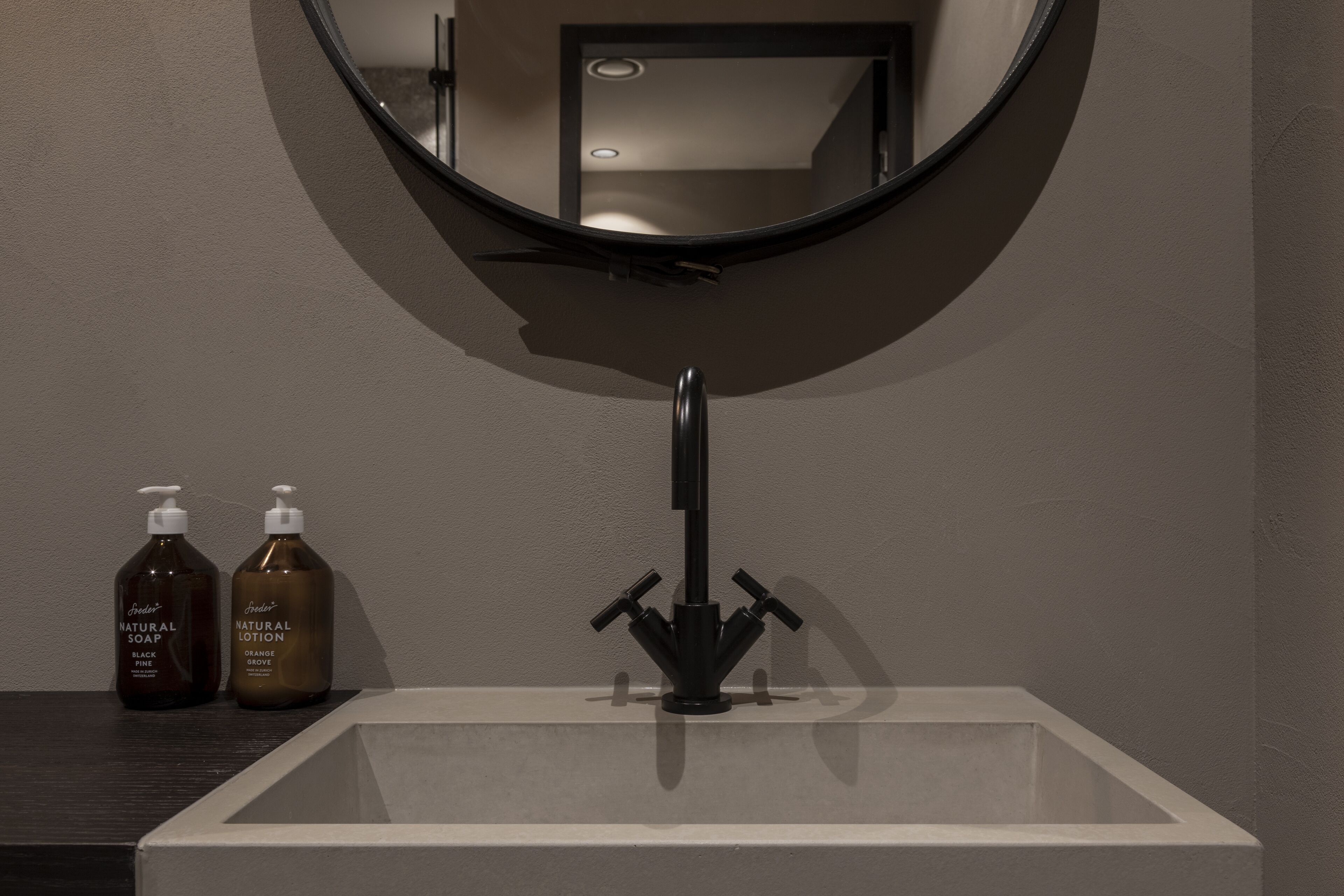 A bathroom with a rectangular sink, a round mirror, and two bottles of soap.