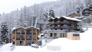 Un moderno complejo de esquí con edificios de varios pisos, fachadas de madera y un entorno cubierto de nieve.