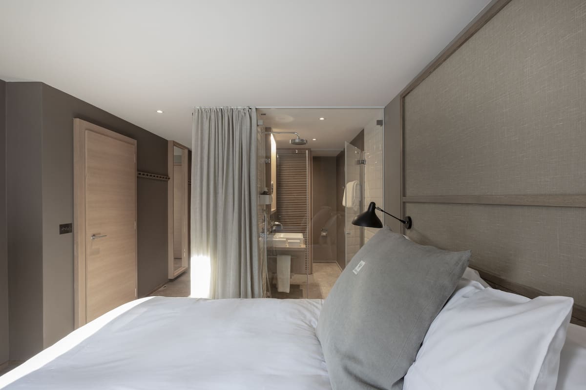 A modern hotel room with a large bed, a bedside table, a lamp, and a view of the bathroom.