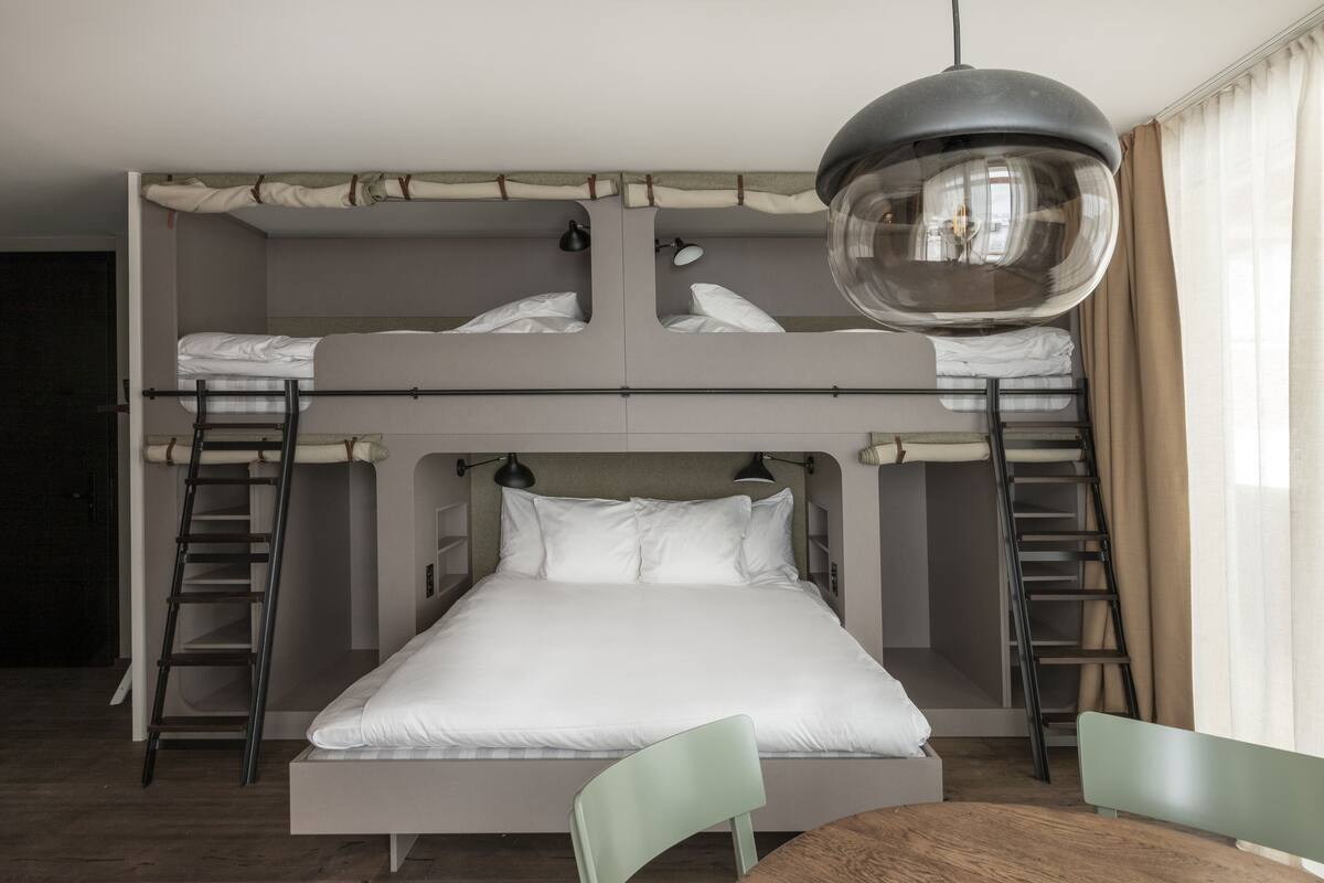 A bunk bed room with a table and chairs, ladders, and a hanging light fixture.