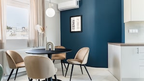 A modern kitchen with a blue accent wall, a round dining table with chairs, and a view of the city through the window. - Iconic 1BR Apartment in Koukaki (Athens)
