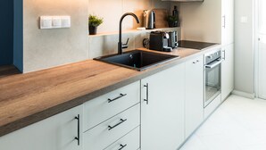 A modern kitchen with white cabinets, a wooden countertop, a sink, a kettle, and a toaster. - Iconic 1BR Apartment in Koukaki (Athens)