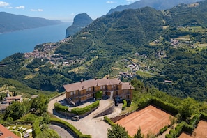 Un grand immeuble à plusieurs étages, doté d’un court de tennis, entouré d’une végétation luxuriante et de montagnes.